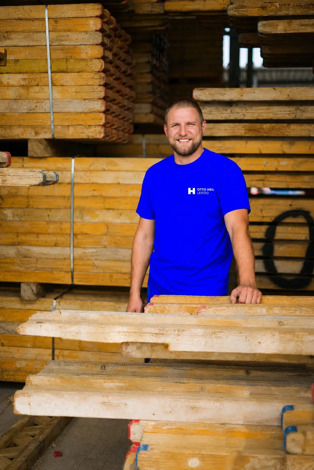 Eine Person steht zwischen mehreren Holzbalken und schaut freundlich in die Kamera