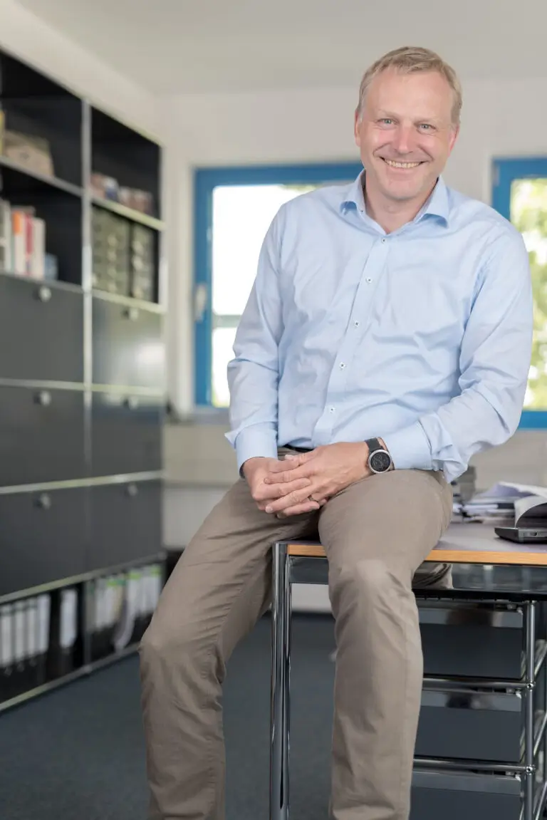 Unternehmer Christoph Heil sitzt am Rand eines Schreibtisches und schaut freundlich zur Kamera